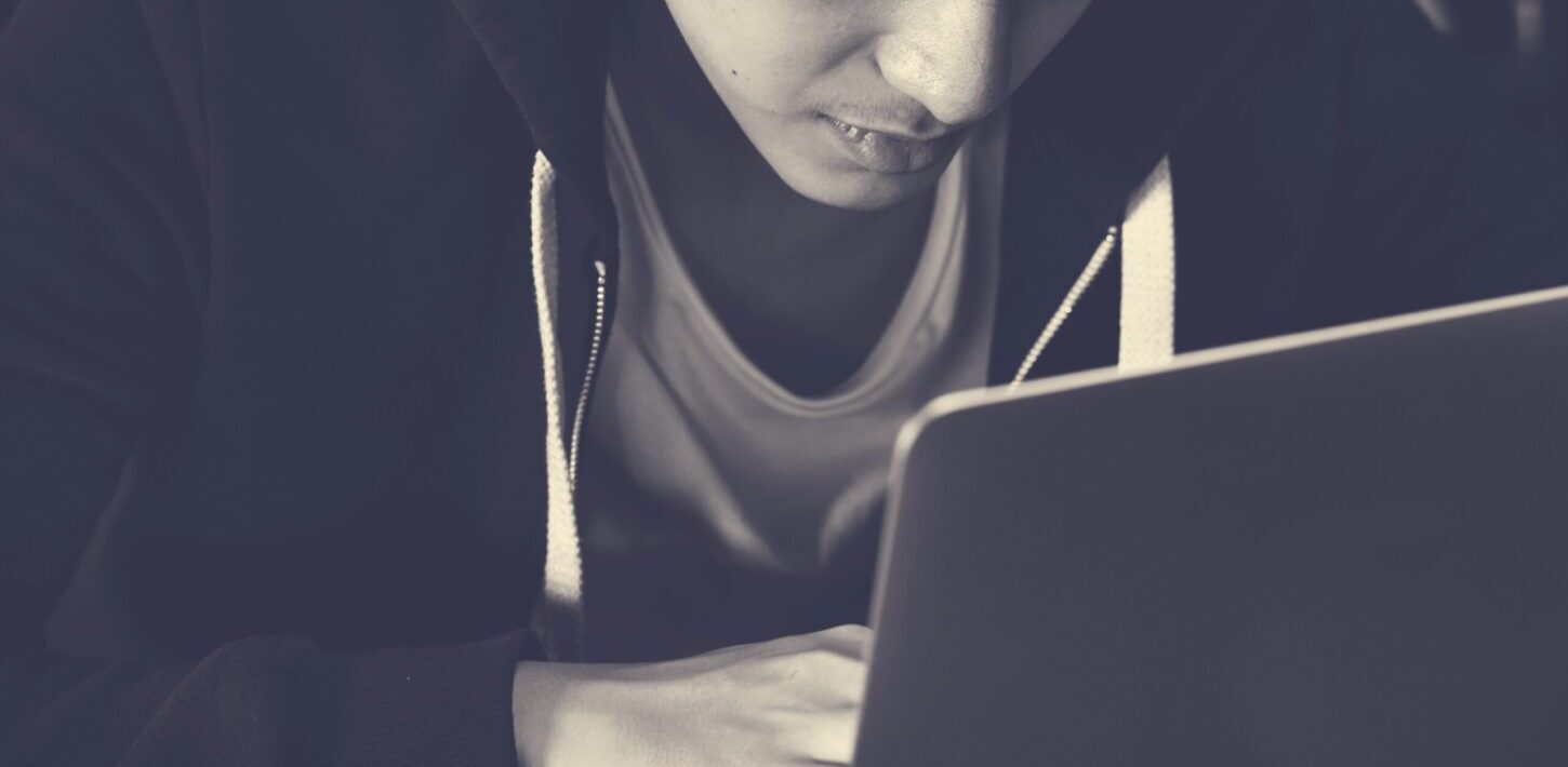 Teen boy in hoodie looking at a laptop screen, representing the issue of online sextortion.