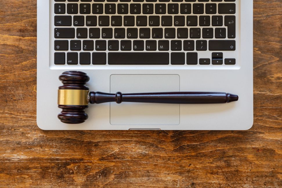 A judge's gavel placed on the keyboard of an open laptop, resting on a wooden surface.