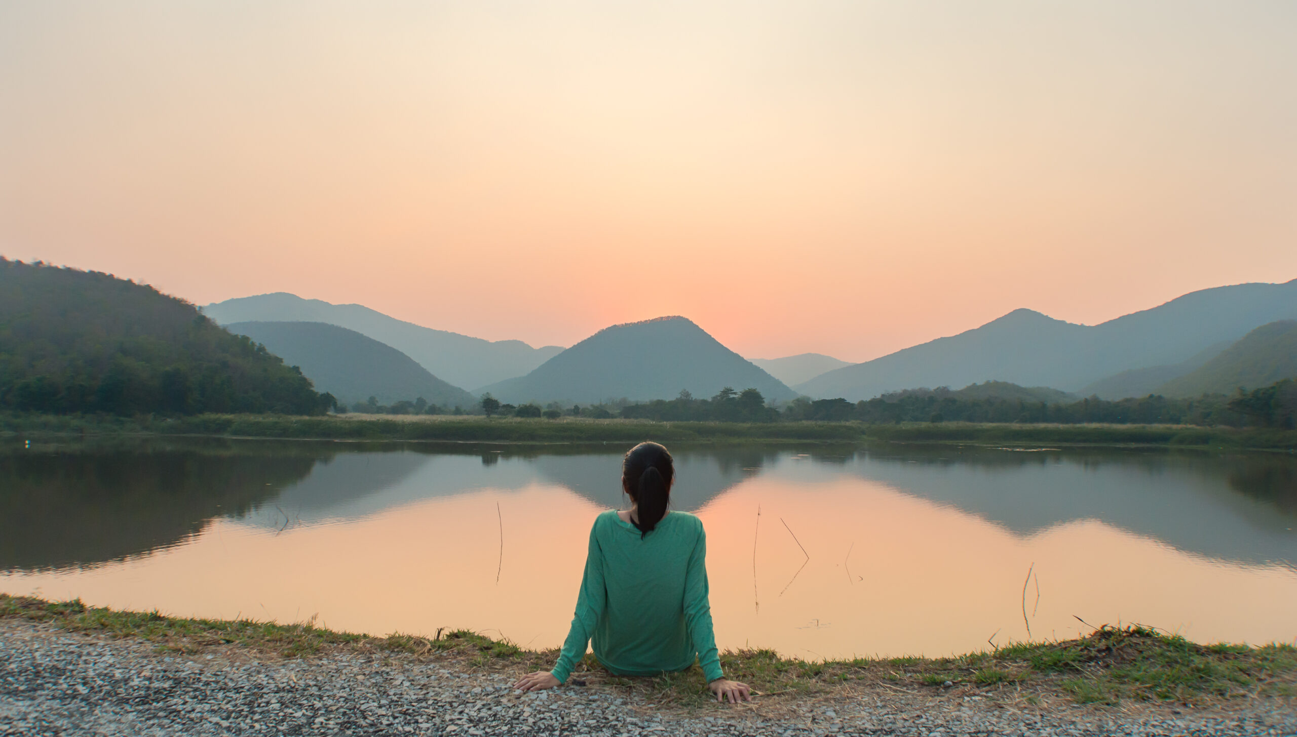 girl sitting on the ground staring on the lake