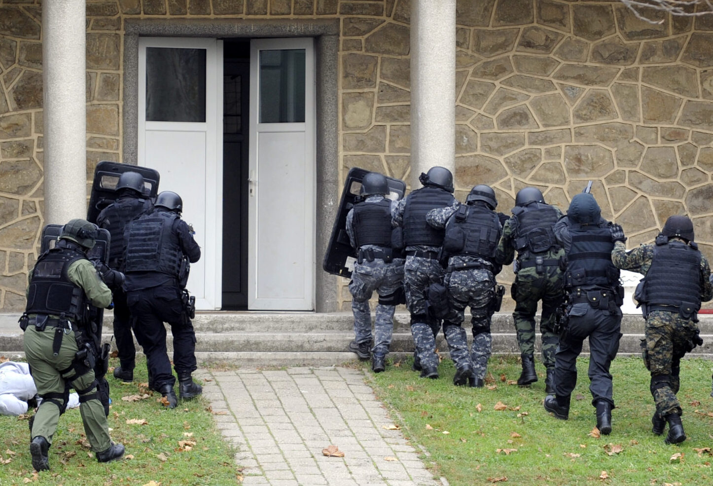 Swat team in tactical gear preparing to enter a building during a swatting incident.