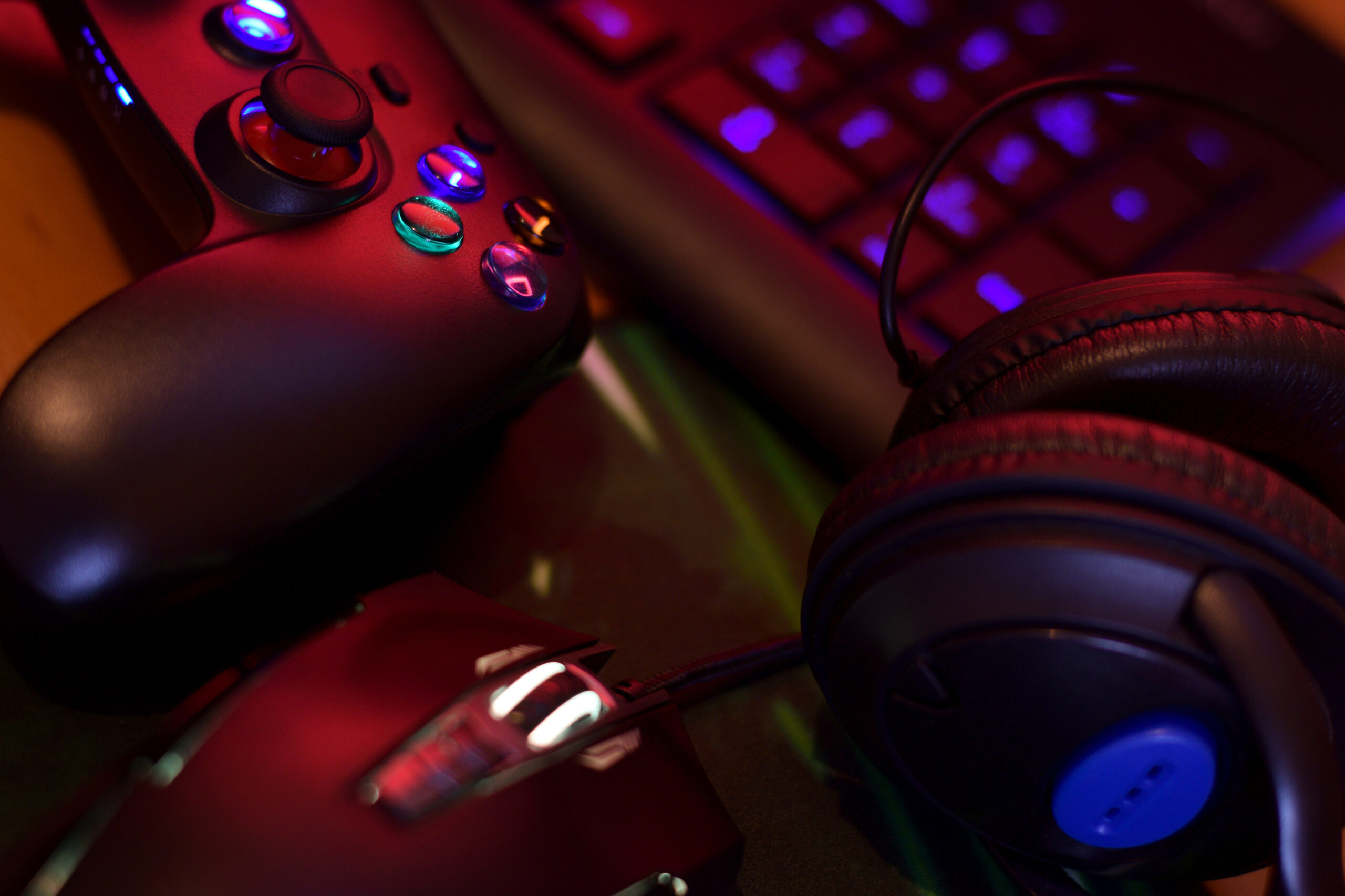 Close-up of a gaming setup featuring a controller, keyboard, mouse, and headphones illuminated by colorful LED lights, representing the dynamic environment of online gaming.