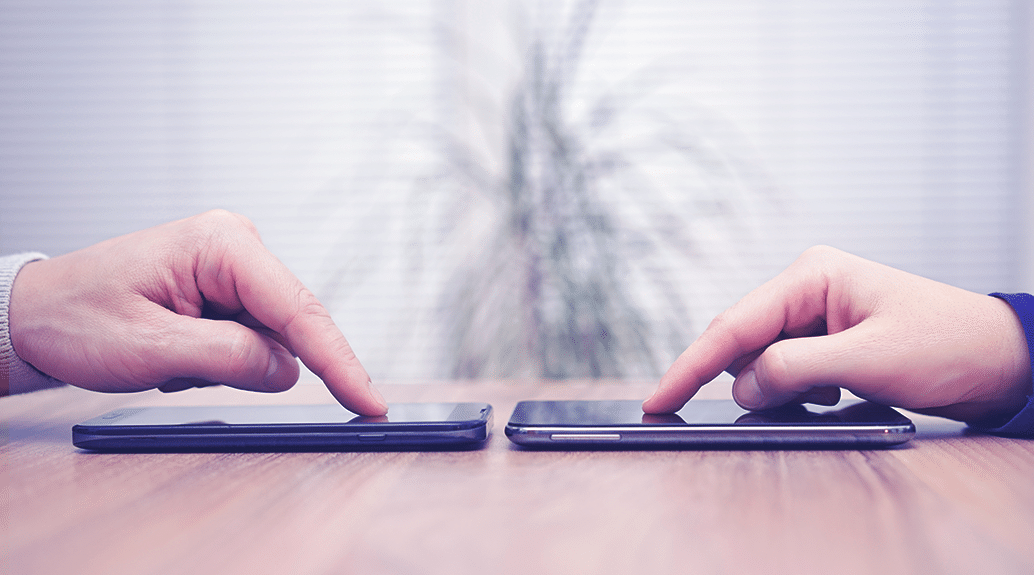 two people pointing at their phones