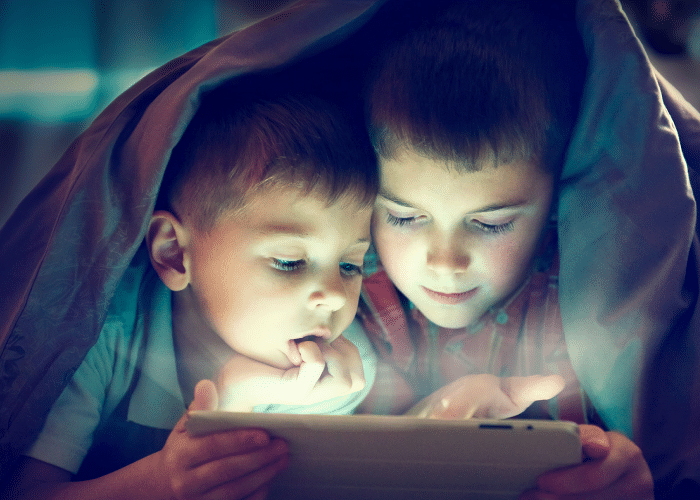 Two young children under a blanket looking at a tablet screen.