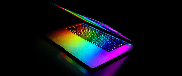 A partially open laptop with rainbow-colored lighting illuminating the keyboard and screen.